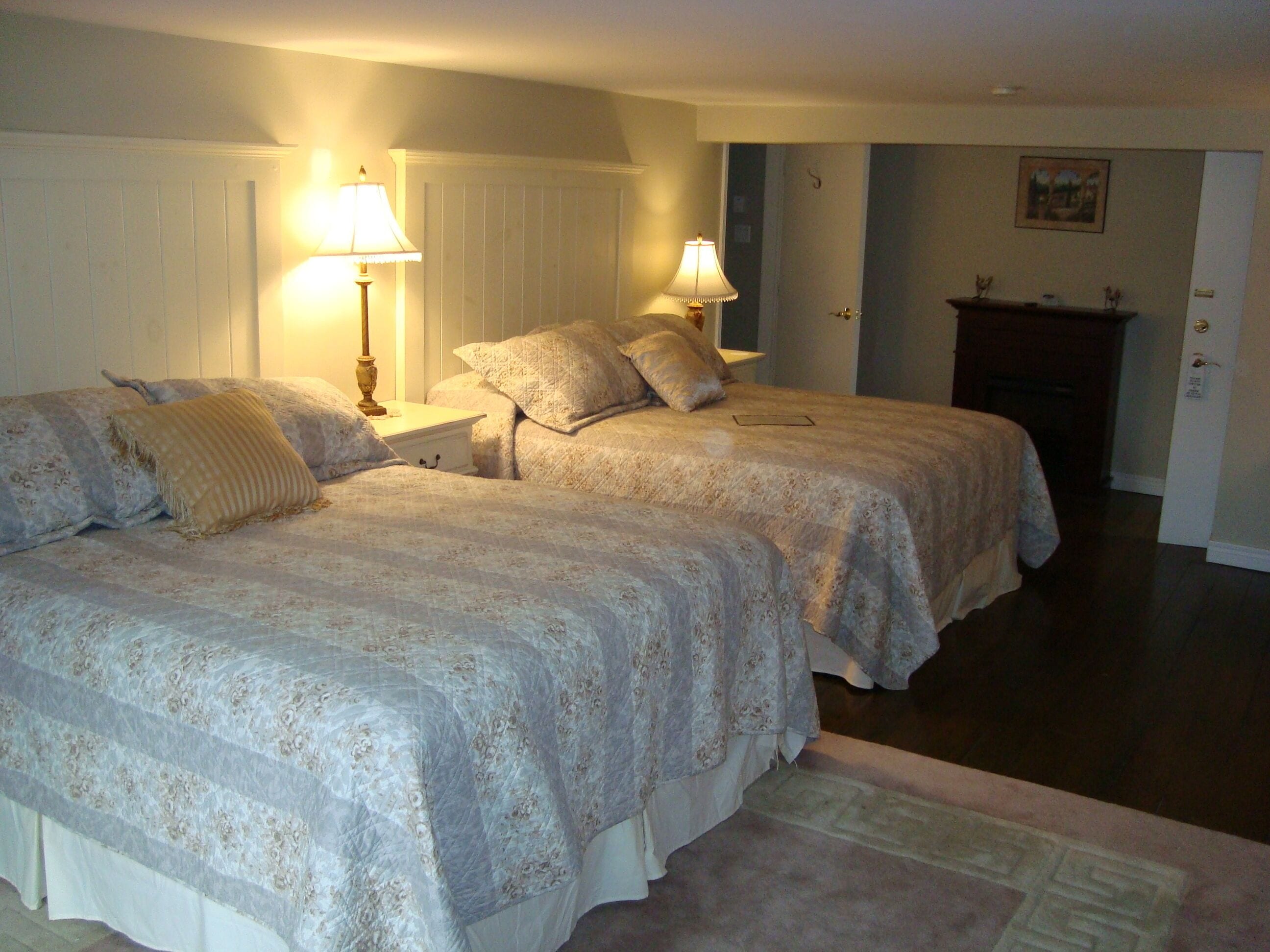 A bedroom with two beds, nightstands, lamps, a fireplace, and a door.