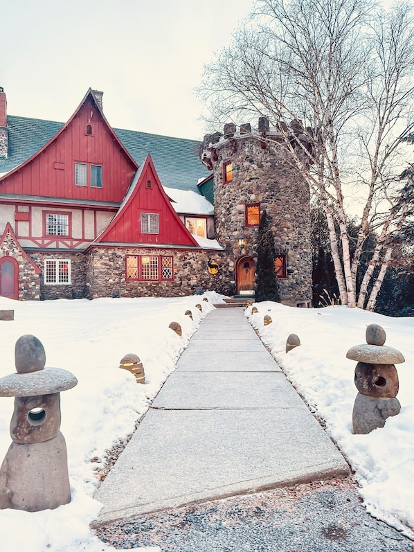 A snow-covered pathway leading to a red barn and a stone building with a turret.