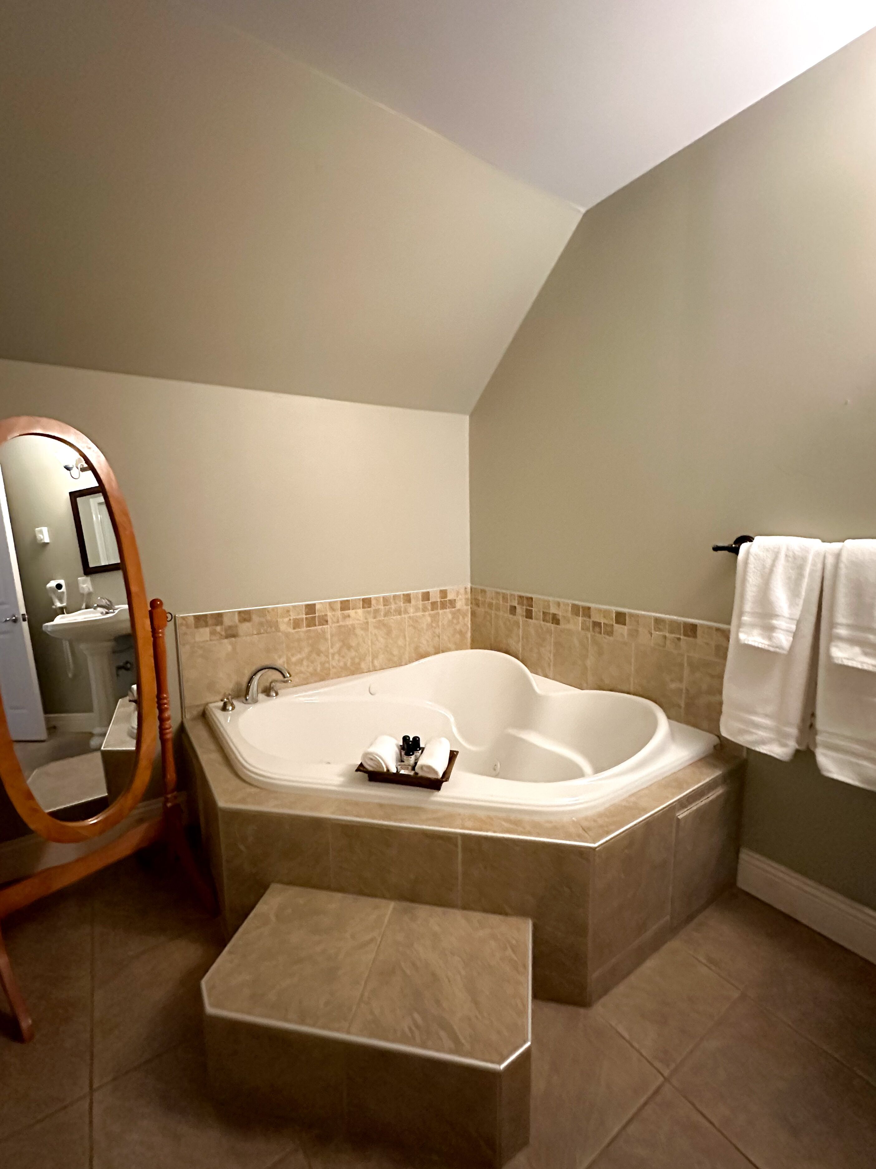 Ein Badezimmer mit freistehender Badewanne, einem Holzstuhl, einem Spiegel und einem Waschbecken.