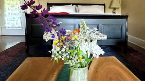 A bedroom with a bed, a nightstand, a vase with flowers, and a painting on the wall.