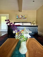 A bedroom with a bed, a nightstand, a vase with flowers, and a painting on the wall.