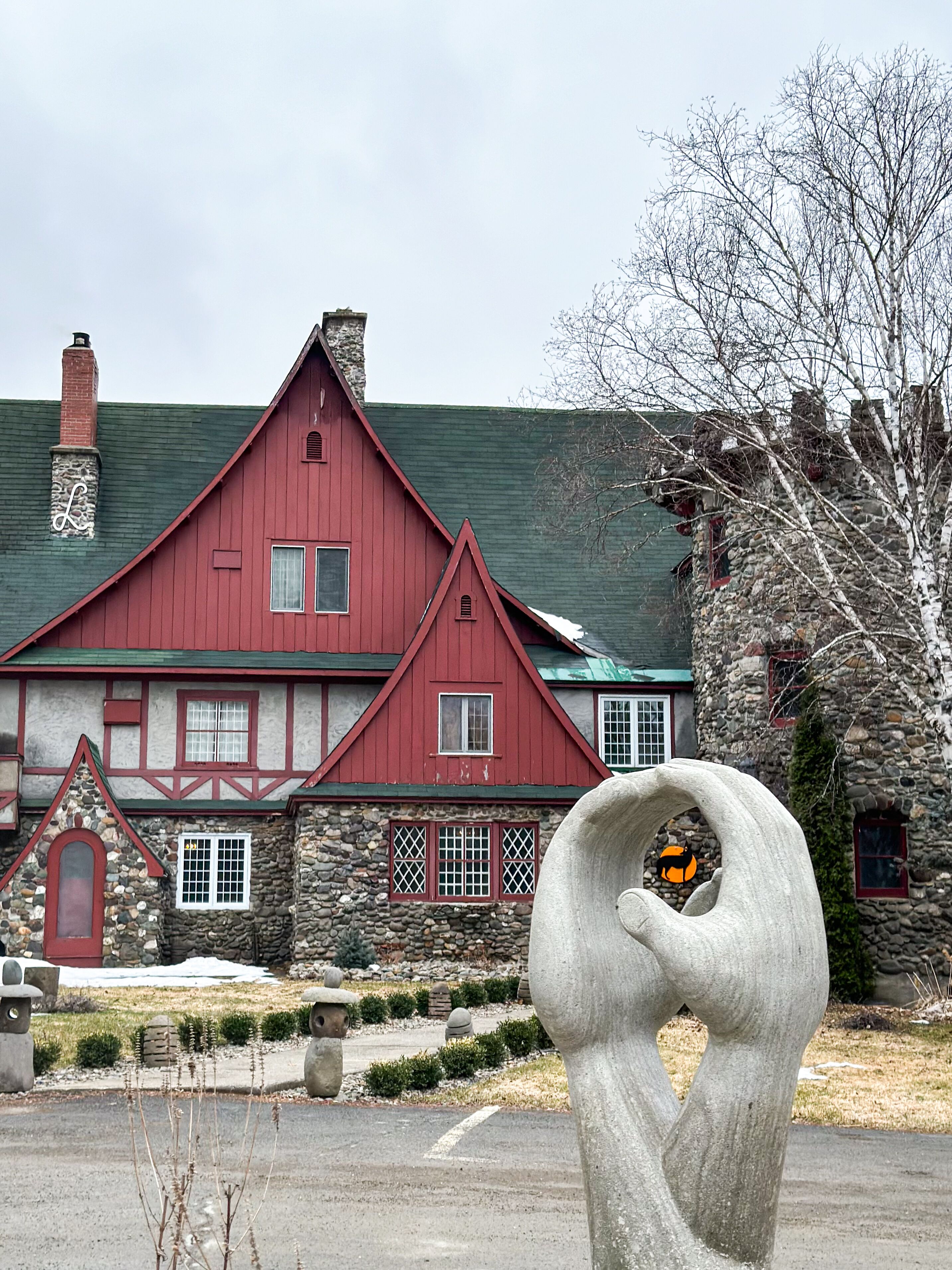 A red building with a stone facade, a chimney, and a stone sculpture in the foreground.