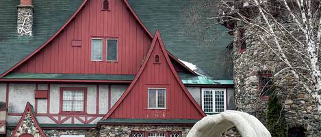 A red building with a stone facade, a chimney, and a stone sculpture in the foreground.