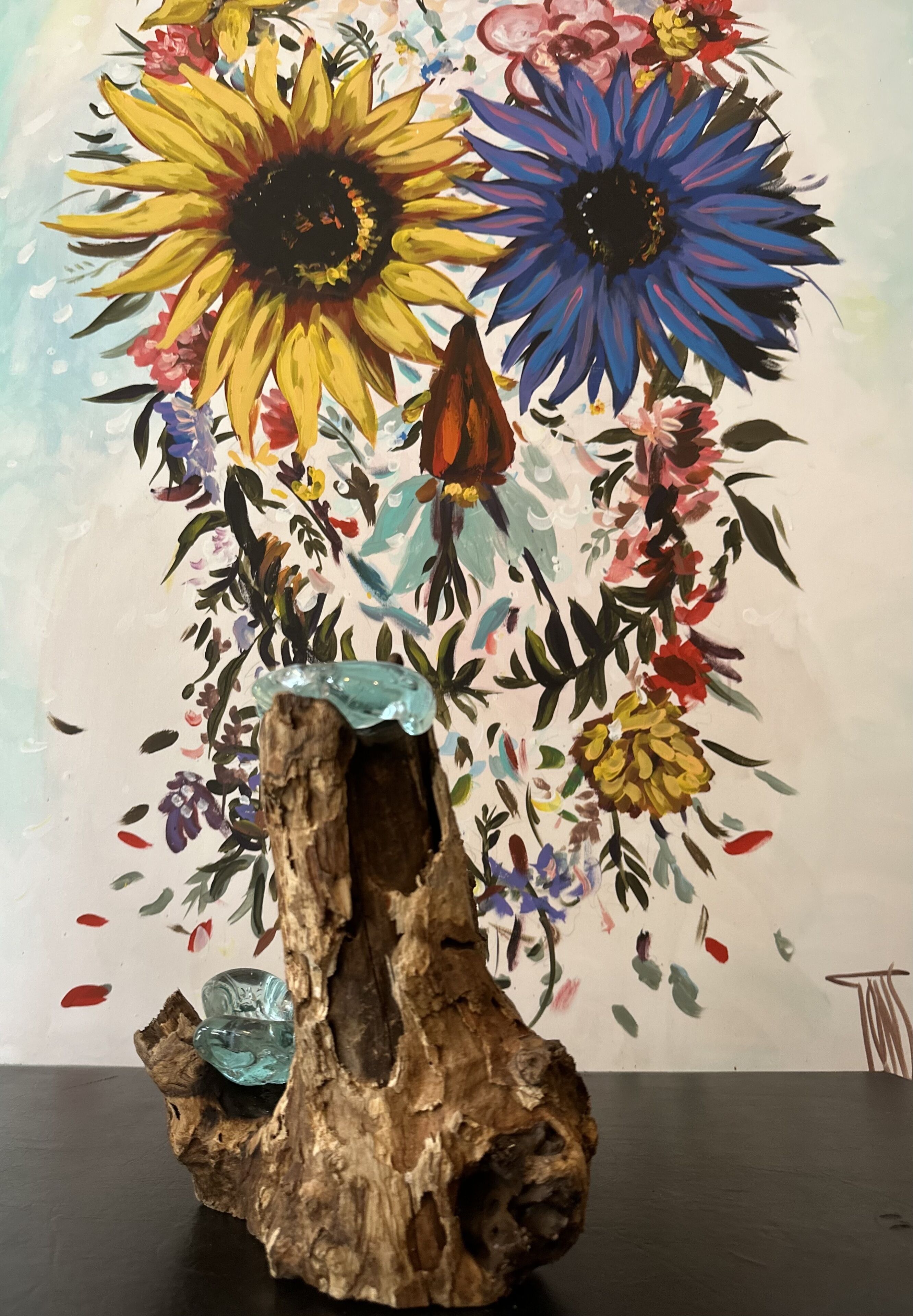 A wooden sculpture with a crystal centerpiece, set against a colorful floral painting.