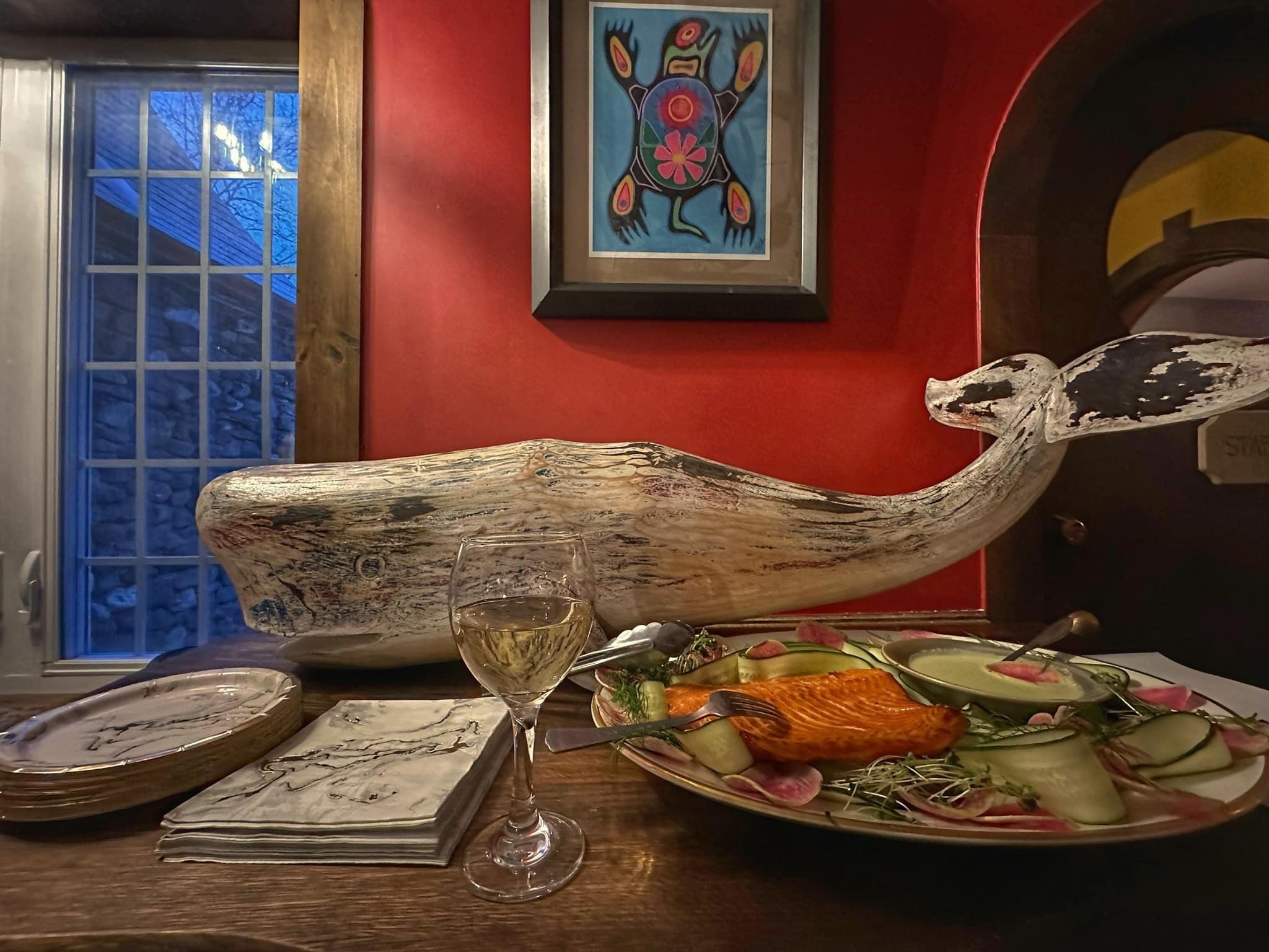 Une table avec un plat de saumon, un verre à vin et une sculpture décorative en forme de tête de baleine.