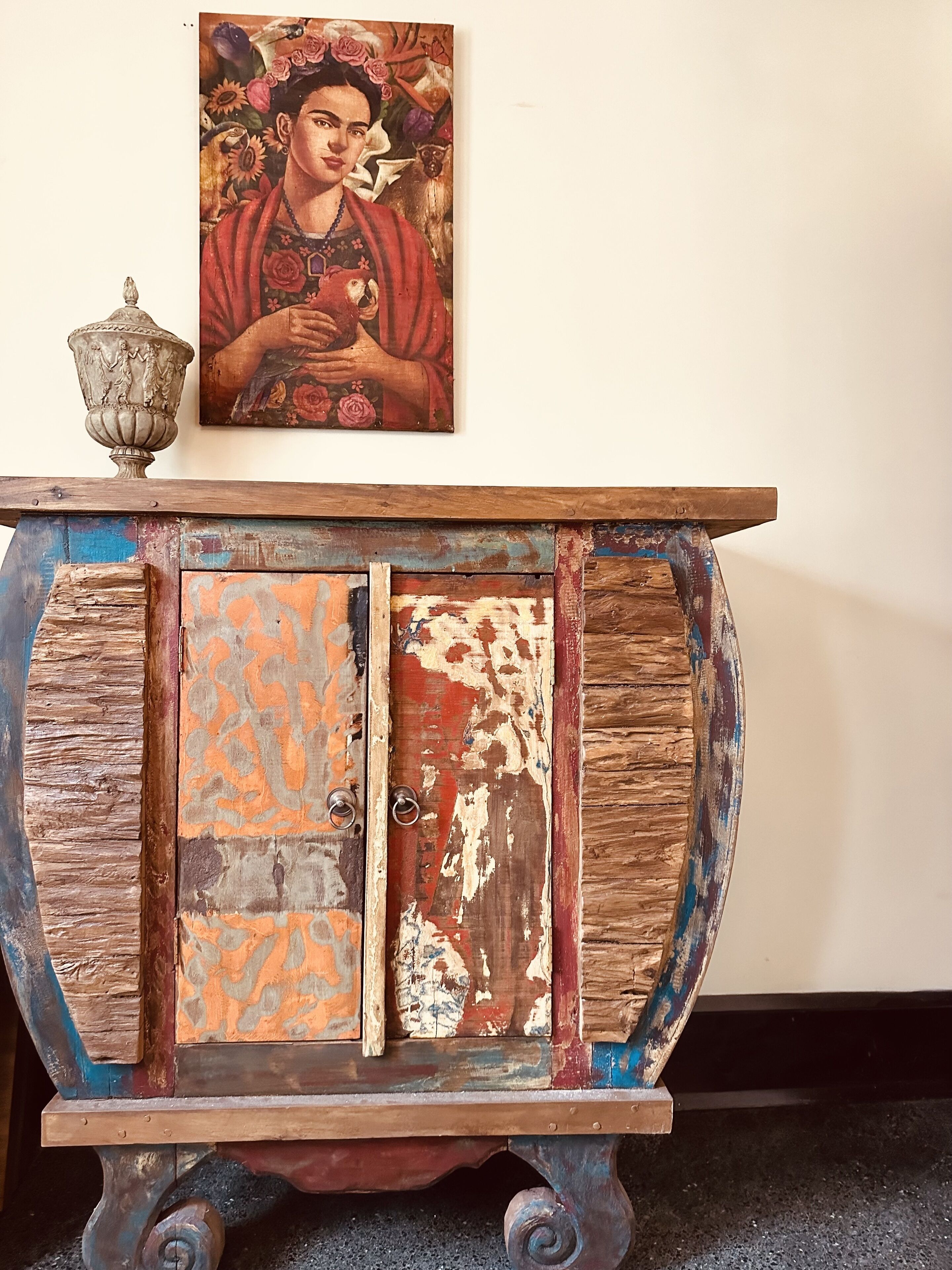 A rustic wooden table with a decorative top and a vintage cabinet with peeling paint.