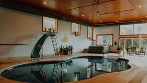 An indoor swimming pool with a wooden ceiling, potted plants, and a ladder.