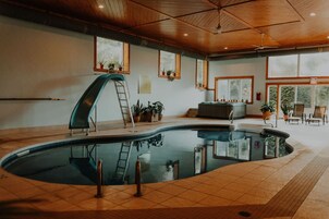 An indoor swimming pool with a wooden ceiling, potted plants, and a ladder.