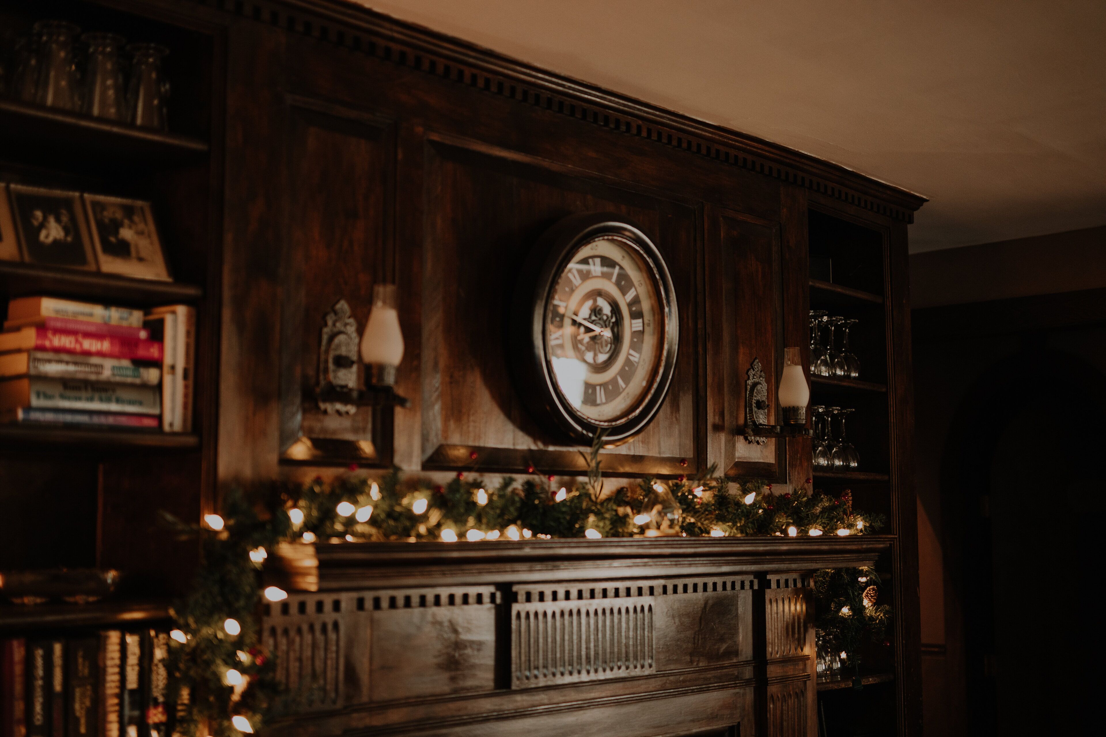 Una repisa de madera con un reloj, estanterías y una guirnalda de luces.