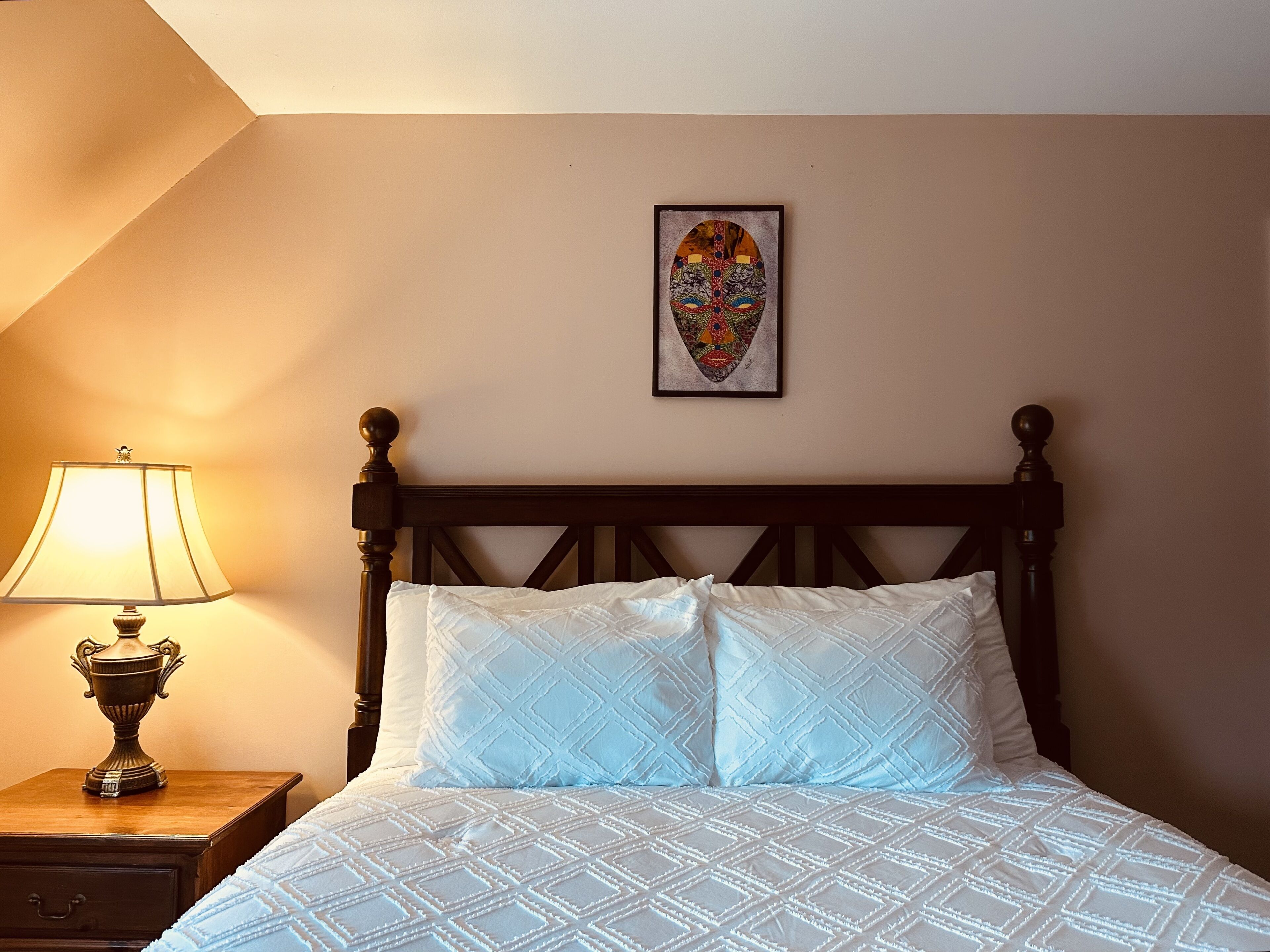 A neatly made bed with a patterned bedspread and two pillows, a bedside lamp, and a framed artwork on the wall.