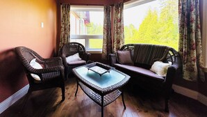 A cozy room with wicker furniture, a glass-top table, and a large window with curtains.