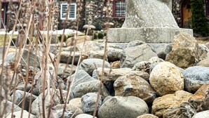 A stone sculpture in a garden with a red building in the background.