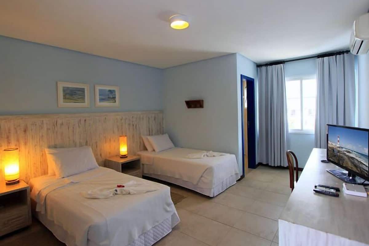 Ein Hotelzimmer mit zwei Betten, einem Schreibtisch mit Computer und einem Fenster mit Vorhängen.