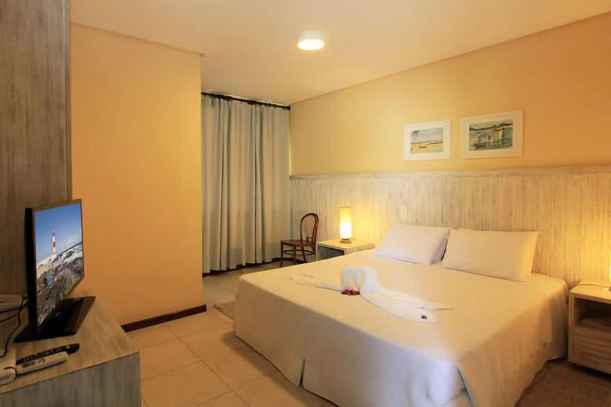 Ein Hotelzimmer mit einem großen Bett, einem Schreibtisch mit Fernseher, einem Sessel und einem Nachttisch.