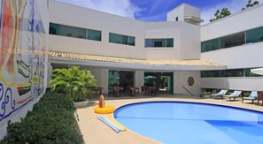 A modern building with a swimming pool, outdoor seating, and a mural. - Farol de Itapuã Praia Hotel (Salvador)