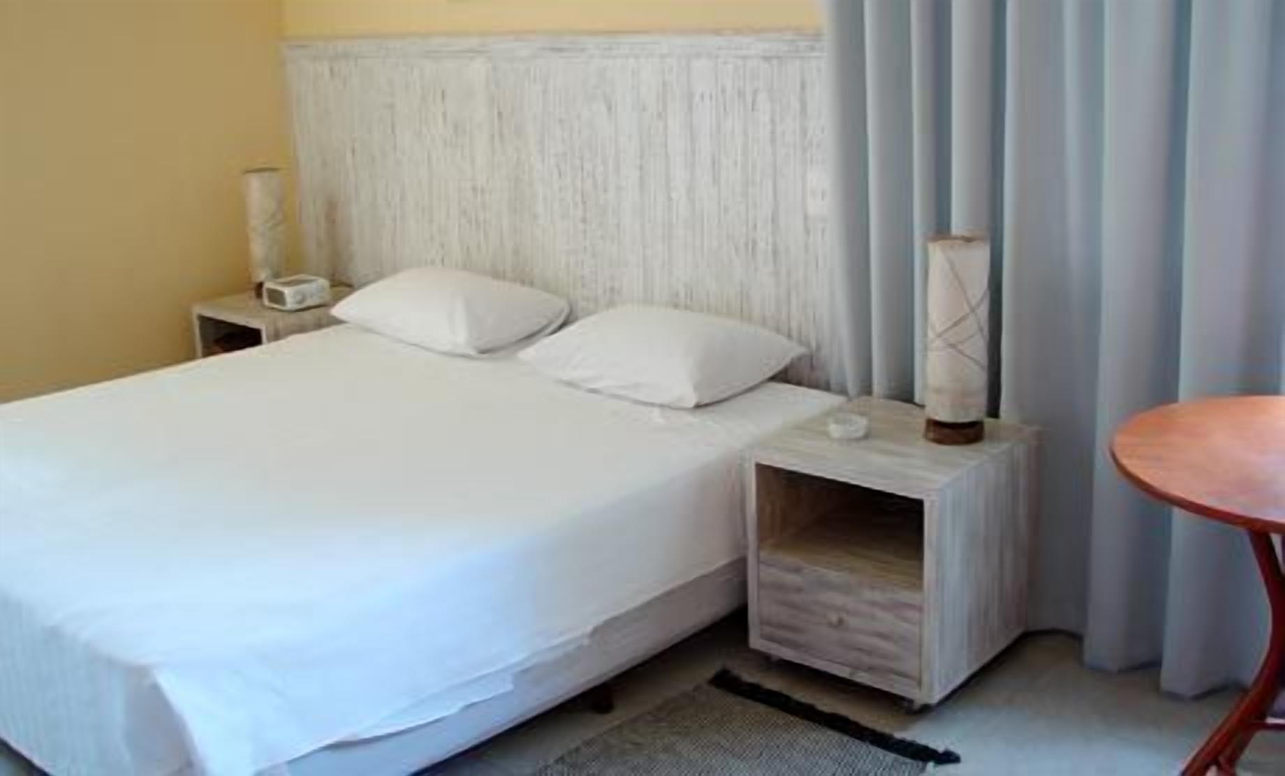 A neatly made bed with white linens, a bedside table with a lamp, and a small round table.
