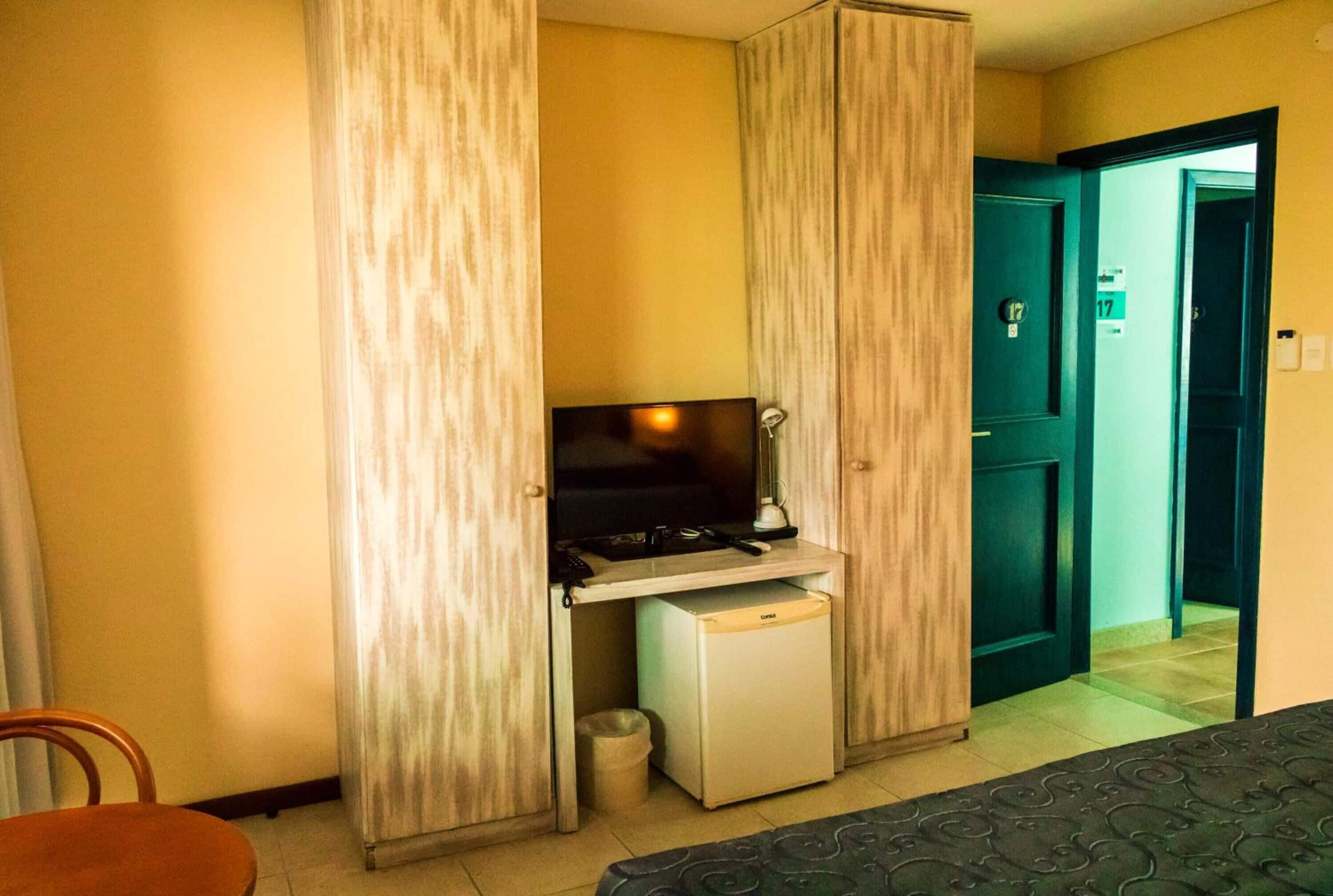 A compact room with a television on a small table, a mini fridge, and a door marked with the number 17.