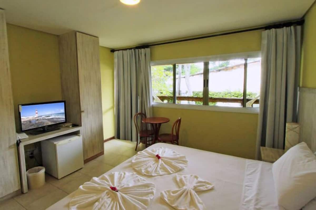 Ein Hotelzimmer mit Bett, Fernseher, kleinem Schreibtisch, Stuhl und einem Fenster mit Vorhängen.