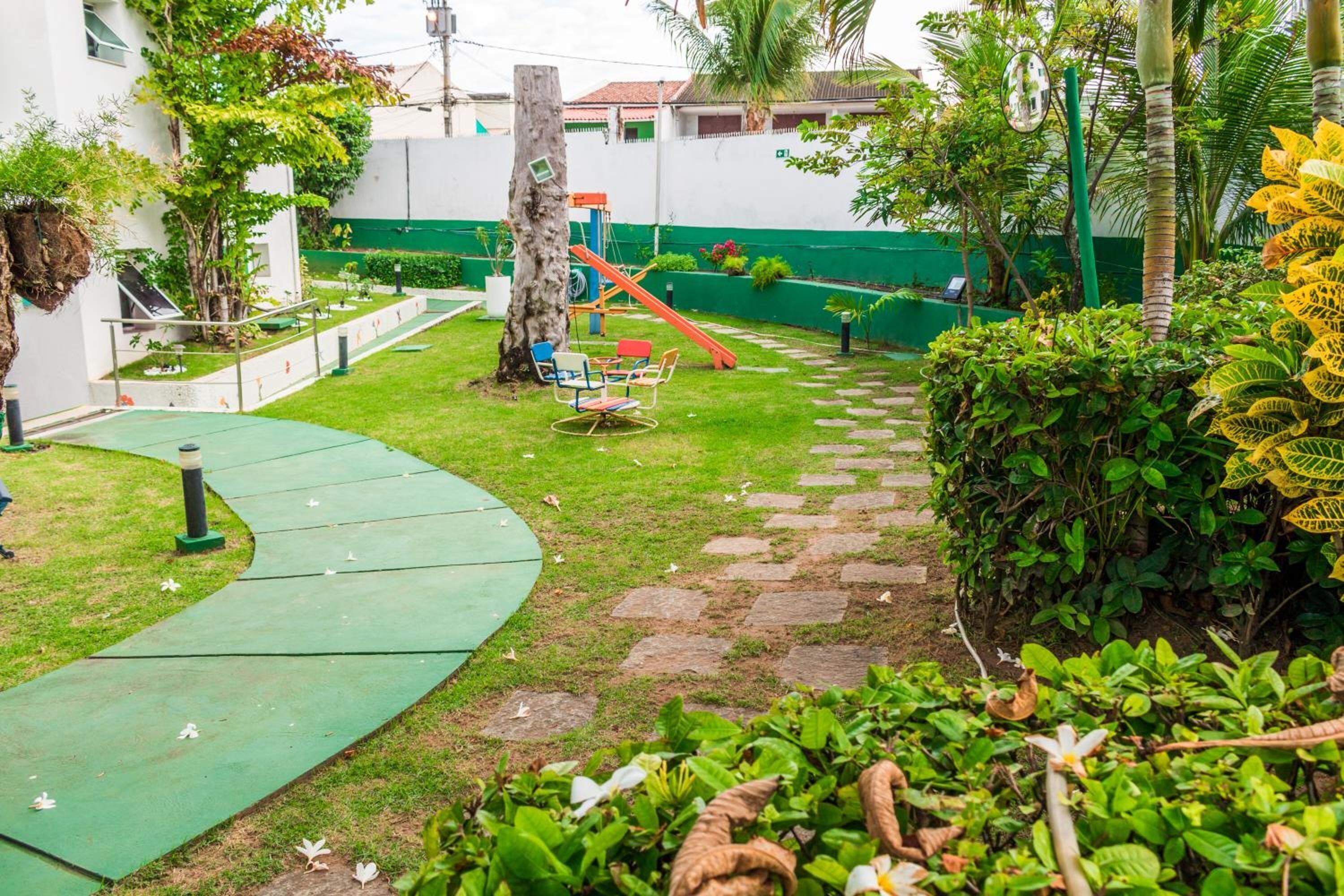 Un jardin avec un chemin bordé de verdure, un toboggan et une petite table entourée de chaises.