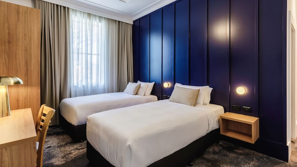 A hotel room with two beds, a desk, and a chair. - Royal Exhibition Hotel (Surry Hills)