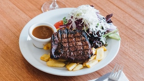 A plate with steak, fries, and salad on a wooden table. - Royal Exhibition Hotel (Surry Hills)