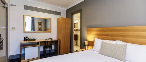 Una habitación de hotel con cama, escritorio con ordenador, espejo y armario.