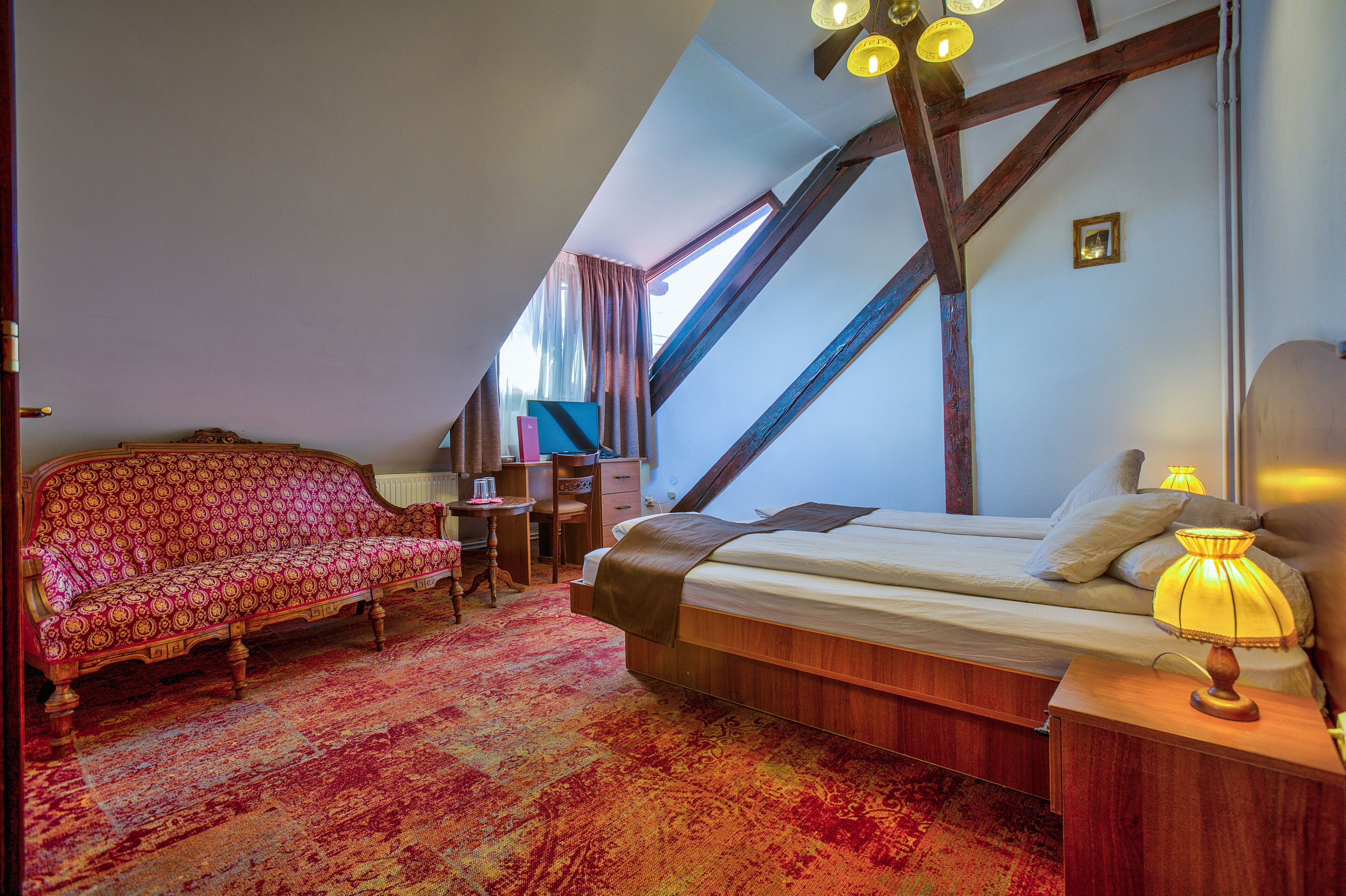 Une chambre avec un plafond en pente, un lit doté d’une tête de lit en bois, un bureau, une chaise et une petite table avec une lampe.