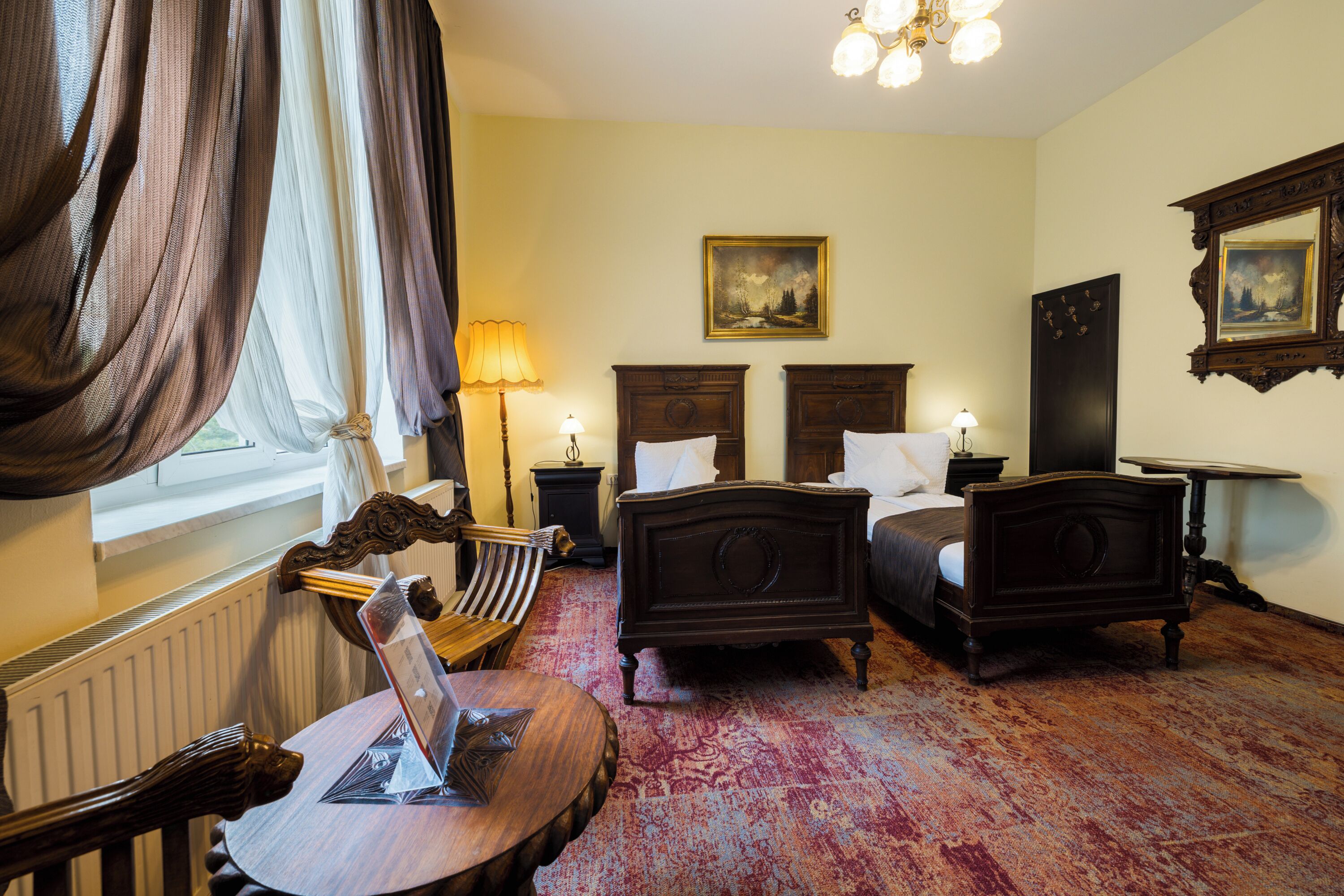 Une chambre traditionnelle avec deux lits simples, une chaise en bois, une table avec une lampe et un grand miroir au mur.