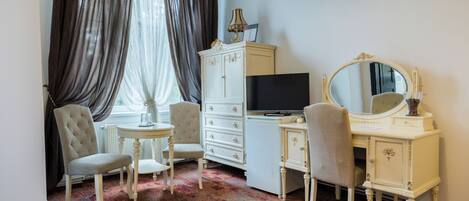 A room with a white vanity, a large mirror, a television, and two chairs.