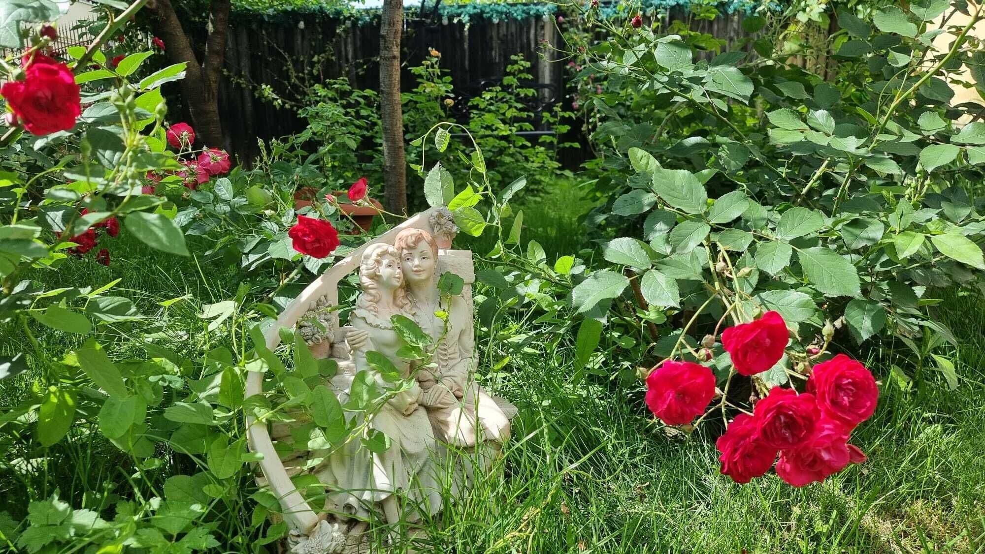 A garden with a statue of a woman holding a child, surrounded by red roses.