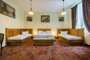 A hotel room with three wooden beds, a large window with curtains, and wall-mounted paintings.