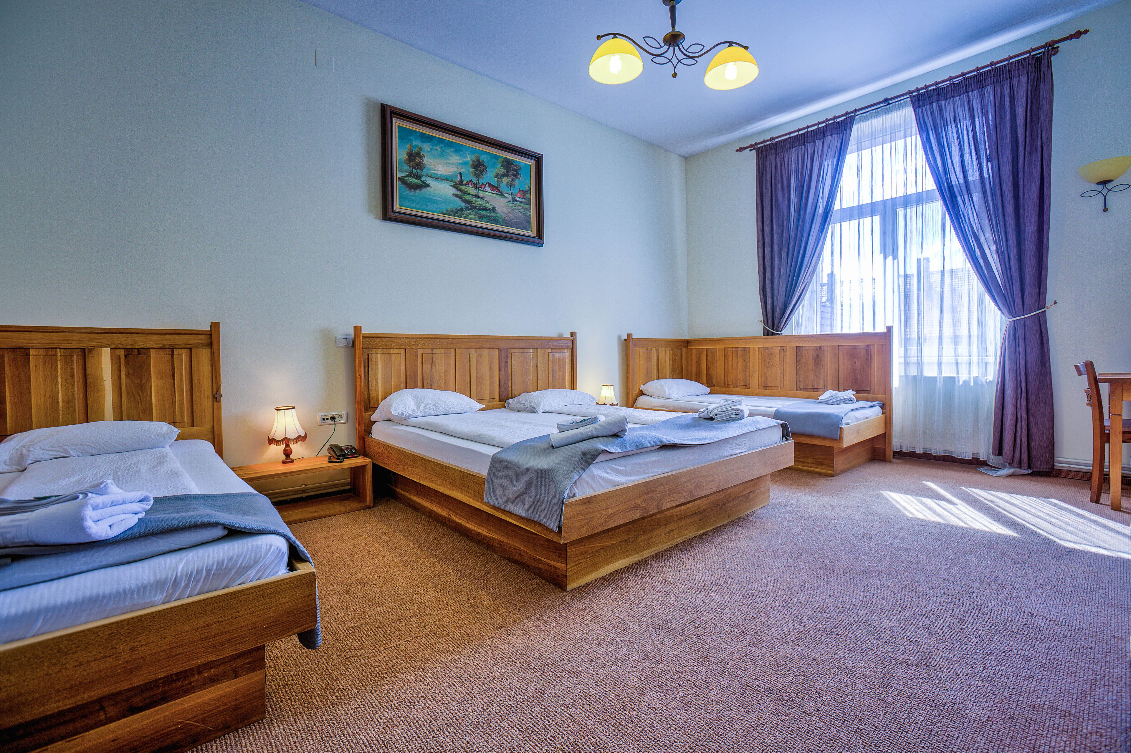 A hotel room with three wooden beds, a painting on the wall, and a chandelier.