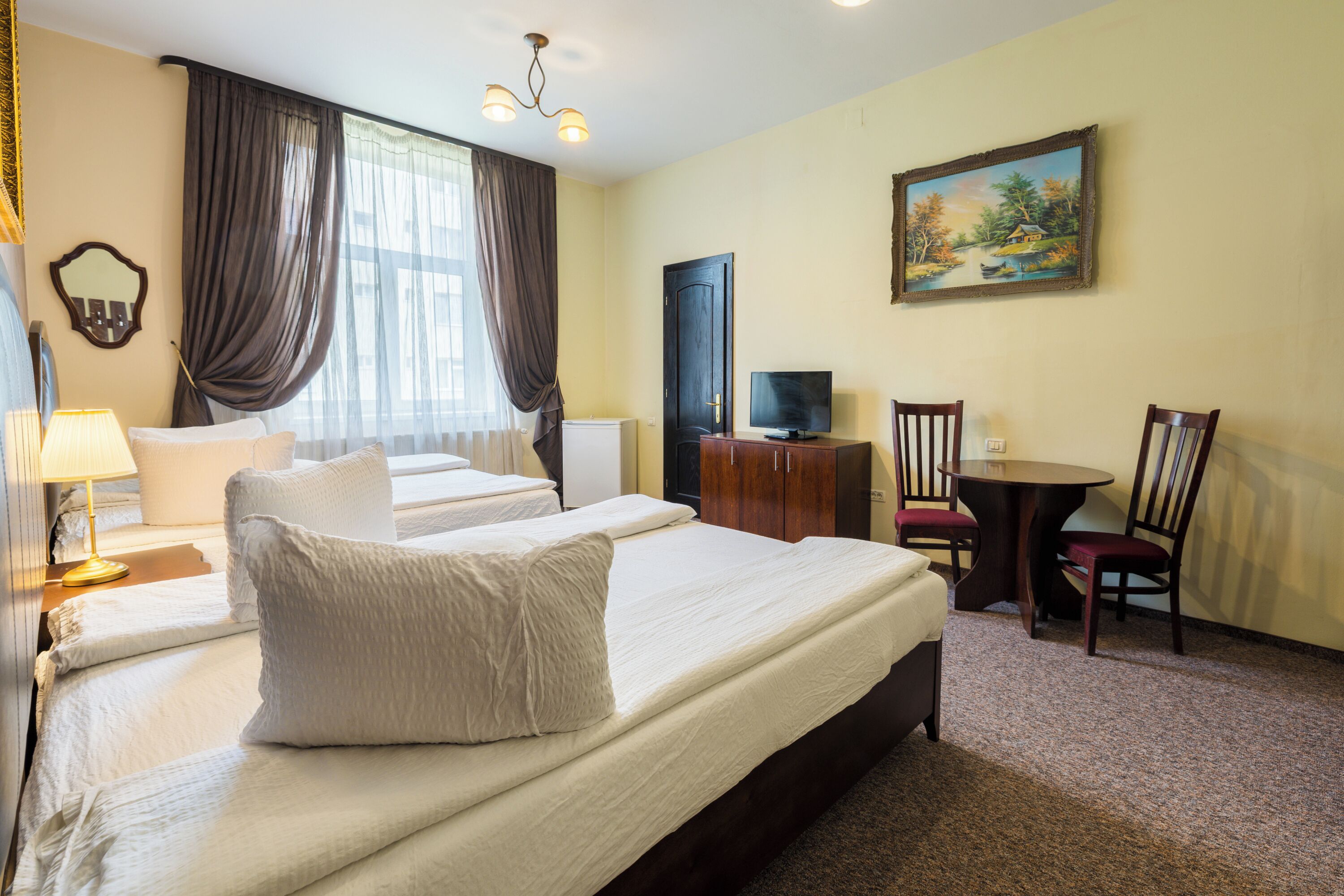 Een hotelkamer met twee bedden, een televisie, een bureau en een schilderij aan de muur.