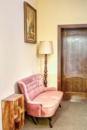 Un sillón rosa, una mesita de madera, una lámpara y una puerta de madera con un número.