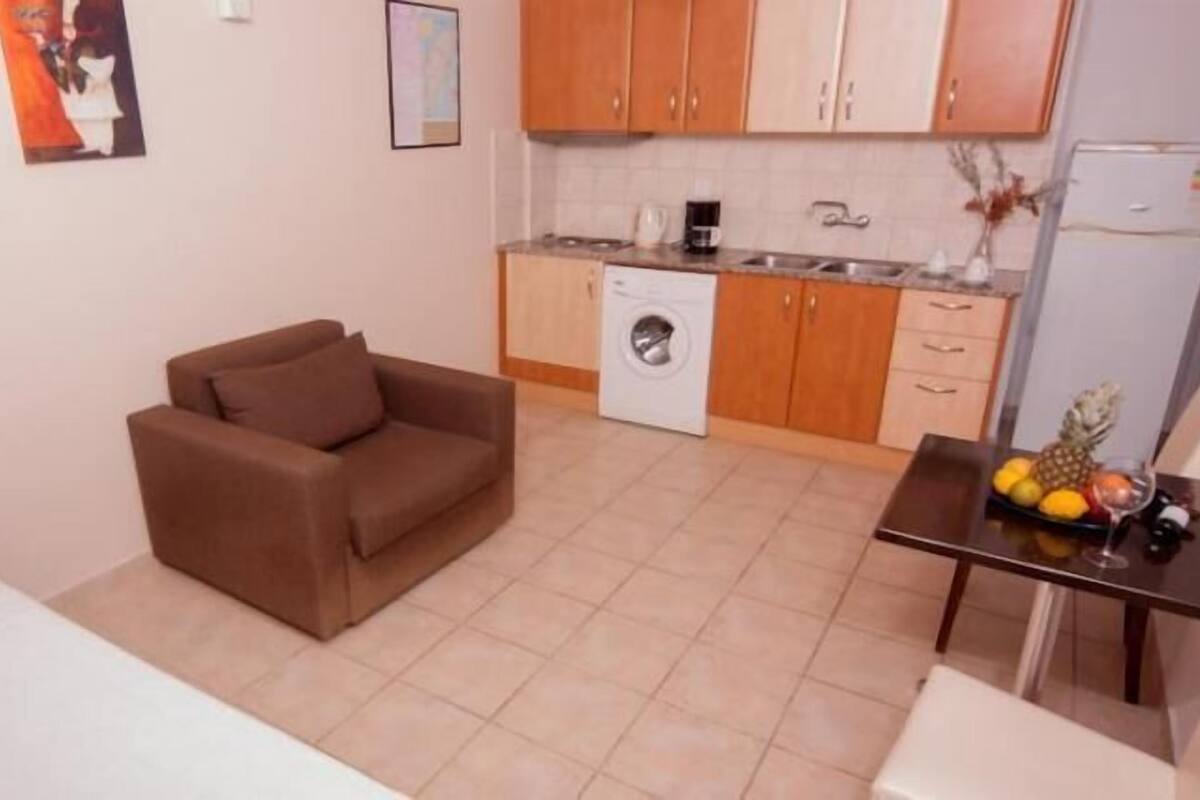 Ein gemütlicher Wohnbereich mit einer Couch, einem kleinen Esstisch mit Früchten, einer Waschmaschine und Holzschränken.