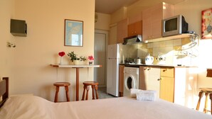 A compact hotel room with a bed, a small kitchenette, a washing machine, and a dining area with stools. - Marika's Aparts & Studios (Rhodes)