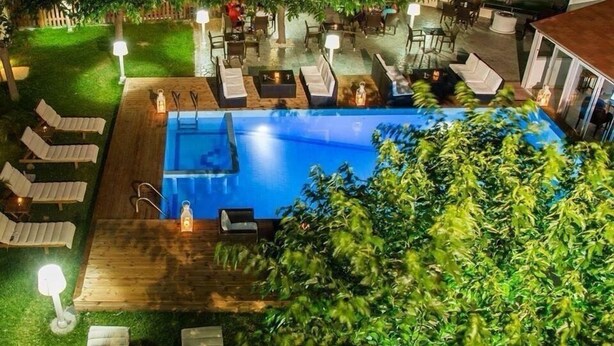 An outdoor swimming pool with lounge chairs and tables, surrounded by a wooden deck and a well-maintained lawn. - Marika's Aparts & Studios (Rhodes)