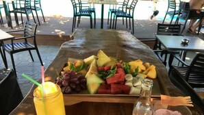A wooden table with a fruit platter, a glass of iced drink, and a bottle of water. - Marika's Aparts & Studios (Rhodes)