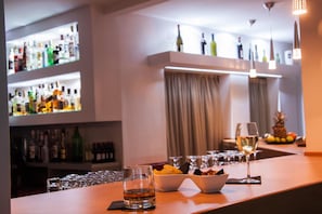 A bar area with shelves of liquor bottles, a bowl of snacks, and glasses of wine. - Marika's Aparts & Studios (Rhodes)
