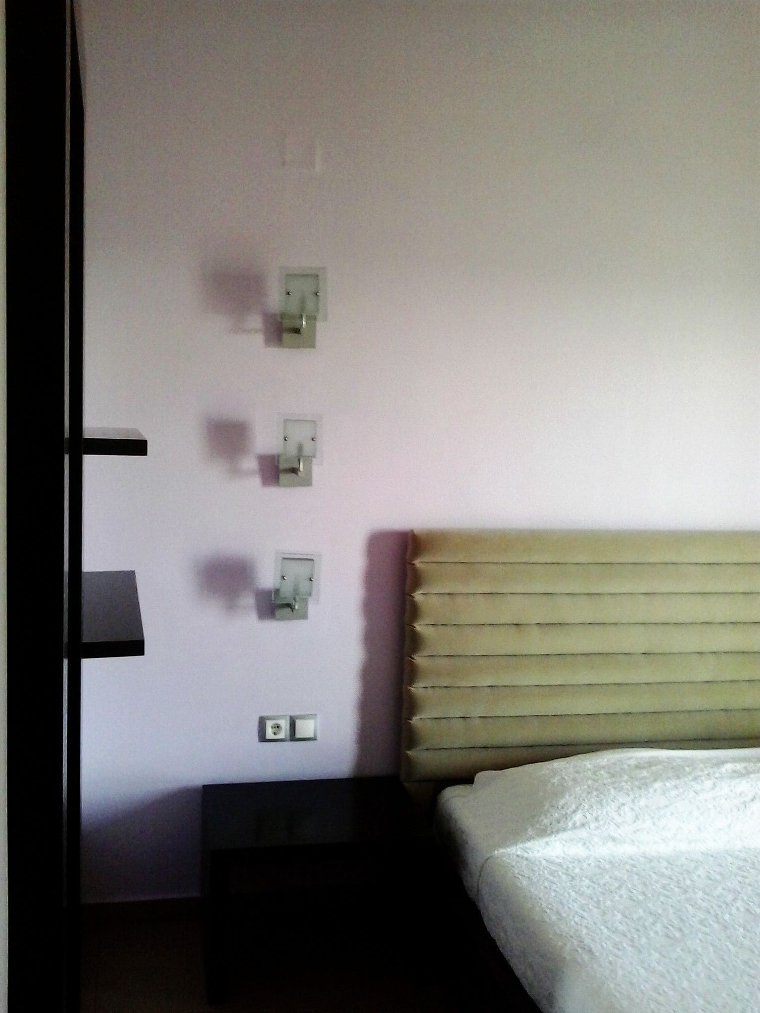 Un dormitorio con cama, una mesita de noche y un interruptor de luz en la pared.