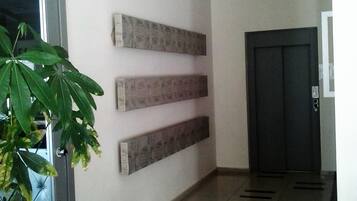 A hallway with a plant, a door, and a wall-mounted panel.