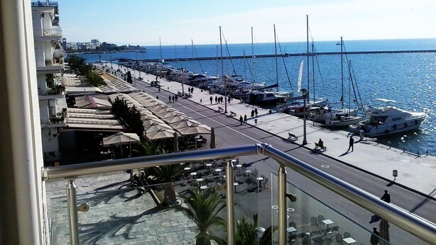 A marina with boats docked along the waterfront, a promenade with outdoor seating, and a view of the sea. - Kipseli Hotel (Volos)