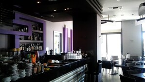A modern bar area with a counter, shelves with bottles, and a seating area with tables and chairs. - Kipseli Hotel (Volos)
