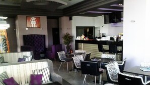 A modern hotel lobby with a seating area featuring sofas and chairs, a bar area with tables and chairs, and a large mirror on the wall. - Kipseli Hotel (Volos)