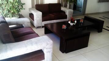 A living room with a brown sofa, a white sofa, and a dark coffee table. There are potted plants and a mirror on the wall.