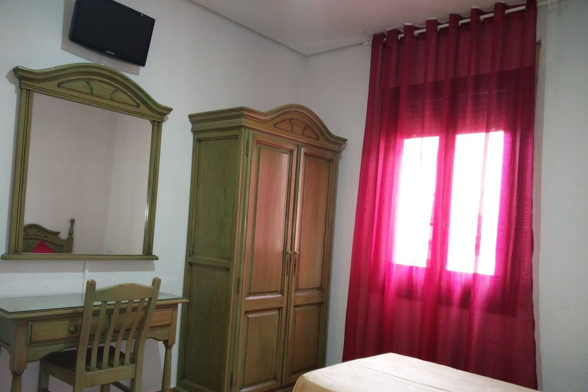 Un dormitorio con cama, escritorio, silla, armario y televisor en la pared.