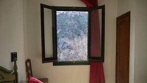 A bedroom with a bed, a window with red curtains, a wooden door, and a small bedside table. - Hotel El Diamantista (Toledo)