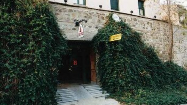 A building entrance with a stone facade, a flag, and a sign. - Hotel El Diamantista (Toledo)