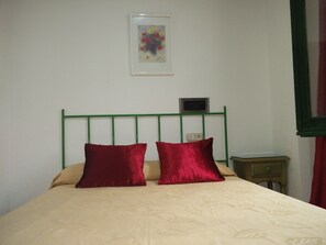 A bed with a green metal headboard, two red pillows, and a beige bedspread with a leaf pattern. - Hotel El Diamantista (Toledo)