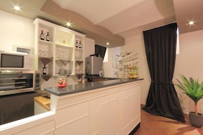 A modern kitchen with white cabinetry, a built-in microwave, wine bottles, and a fruit bowl on the counter. - Hotel Ferrucci Firenze (Florence)